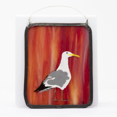 A bold seagull design hand-painted on a piece of rich red-orange streaked stained glass with a waxed lead border and hanging wire.