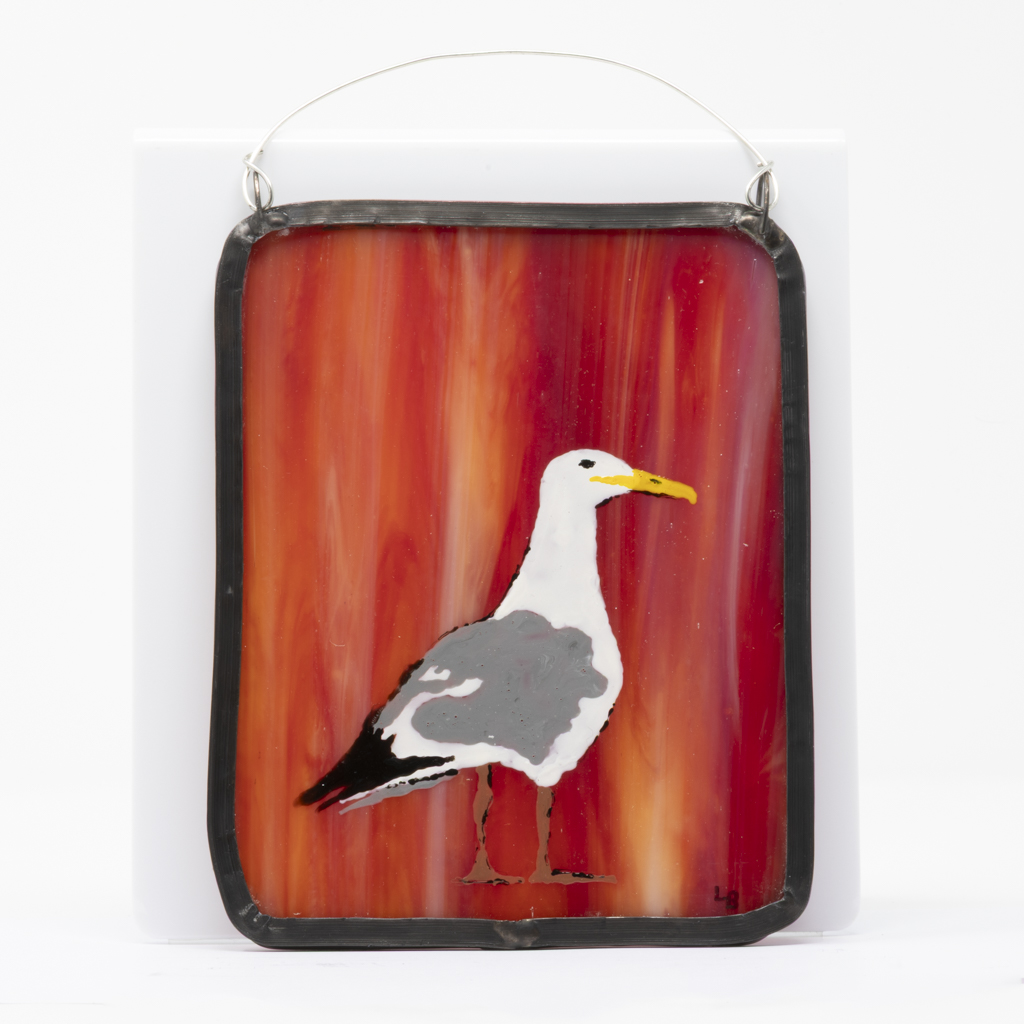 A bold seagull design hand-painted on a piece of rich red-orange streaked stained glass with a waxed lead border and hanging wire.