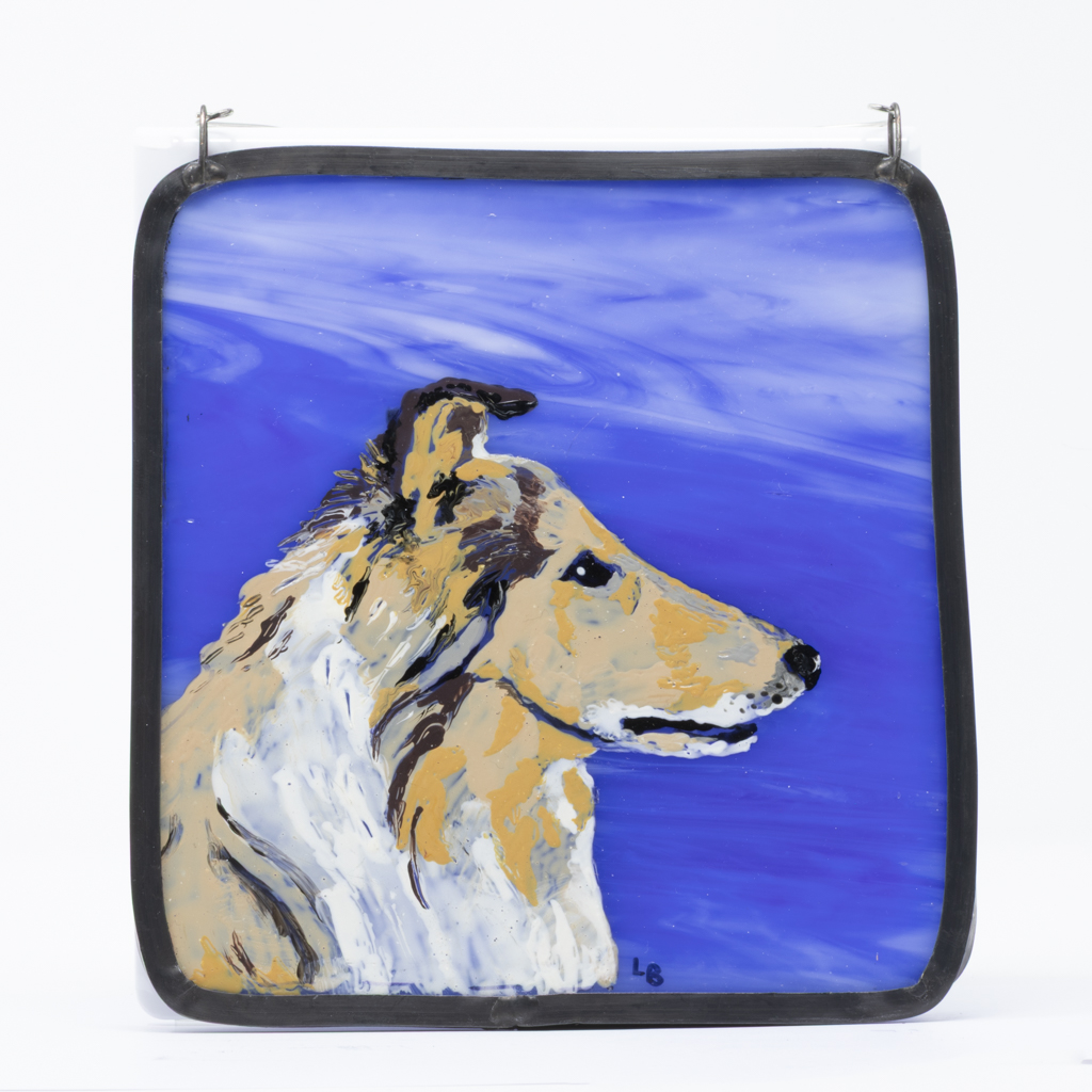 A wall art piece featuring a hand-painted Rough Collie head in profile painted on a piece of rich blue and white stained glass and framed with real lead came that has been blackened and waxed. Wire hanger attached to the top.