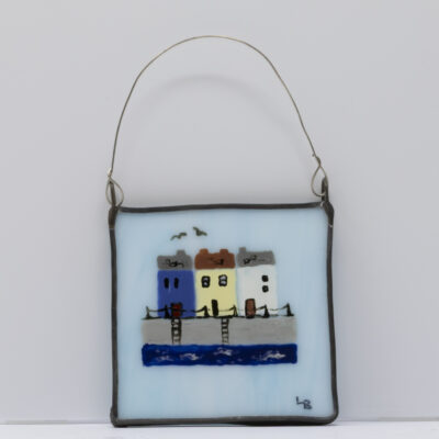 A cute little wall art piece featuring fishermen's cottages overlooking a harbour hand-painted on a pale blue piece of real stained glass.