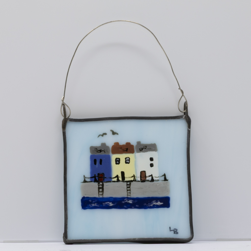 A cute little wall art piece featuring fishermen's cottages overlooking a harbour hand-painted on a pale blue piece of real stained glass.