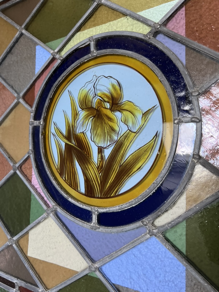 Close-up of original hand-painted iris design in circle of blue glass in centre of Victorian stained glass window.